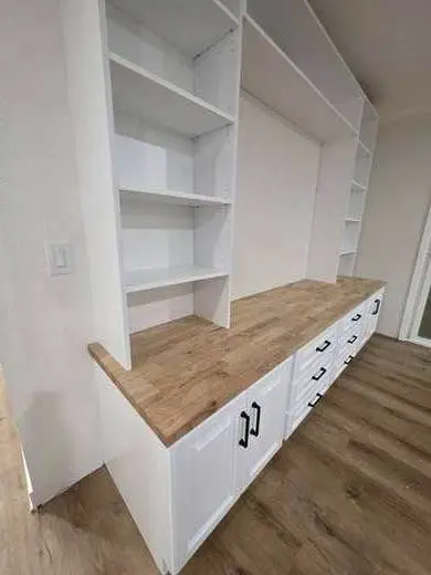 Custom white built-in wall unit with open shelves, drawers, and a butcher-block counter