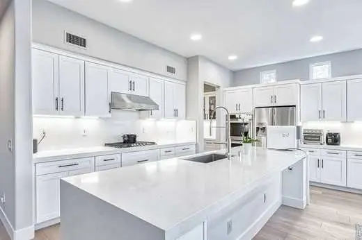 Custom all-white Shaker kitchen cabinets with black hardware and a quartz island