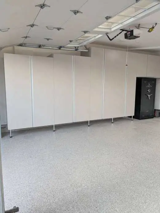 Custom off-white floor-to-ceiling garage cabinets on adjustable legs with an epoxy flake floor