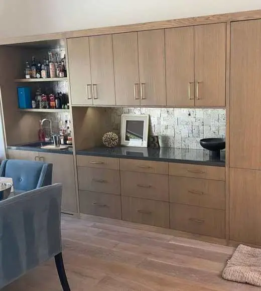 Custom wood-tone home bar with open display shelving, a black countertop, and gold hardware