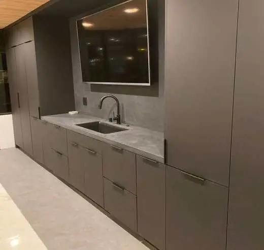 Detail of custom charcoal gray cabinetry wet bar with a sink, TV niche, and black hardware