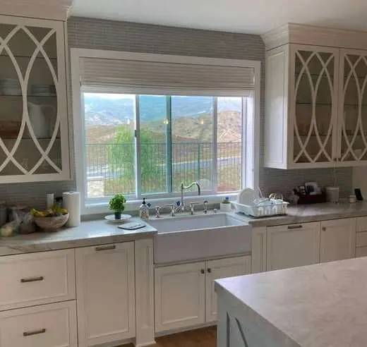 Custom white kitchen cabinets with decorative glass-front upper doors above a farmhouse sink