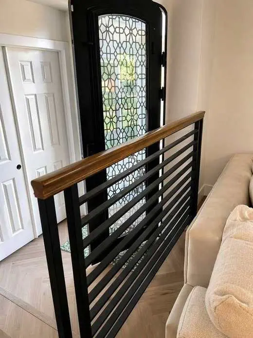 Custom wood-topped stair railing next to a decorative wrought iron and glass entry door