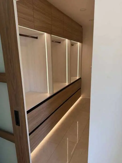 Custom white oak walk-in closet with LED shelf lighting, drawer stacks, and hanging rods