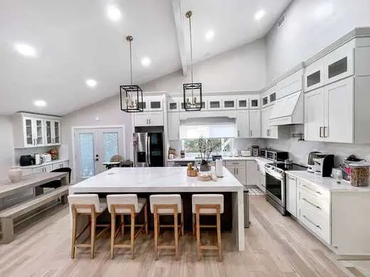 Custom white kitchen with a marble waterfall island, vaulted ceiling, and stainless appliances