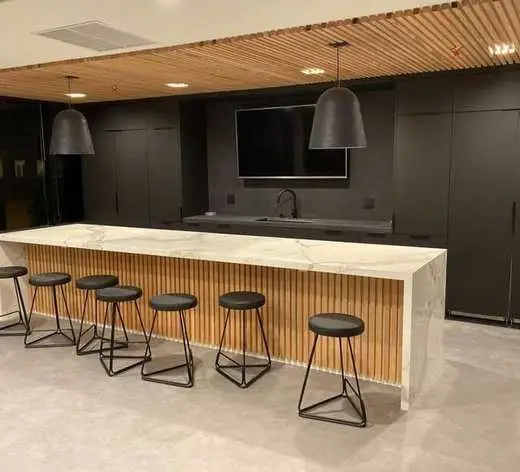 Custom charcoal gray cabinetry with a light marble waterfall island, wood slat accent wall, and black pendant lighting