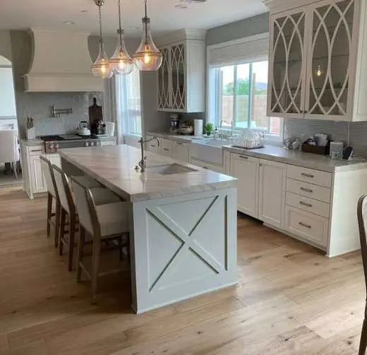 Custom white kitchen cabinets around a range and hood, with an X-pattern island and nickel hardware