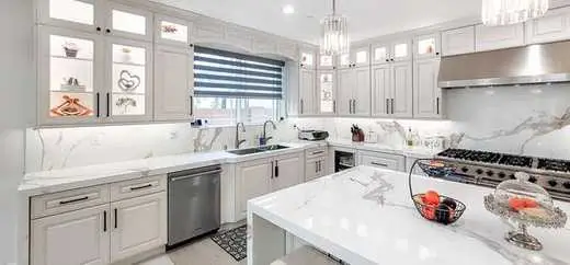 Custom white kitchen with glass-front upper cabinets, black hardware, and marble counters and backsplash