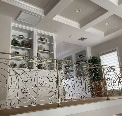 Custom white built-in shelving in a loft hallway with a decorative wrought iron and gold railing