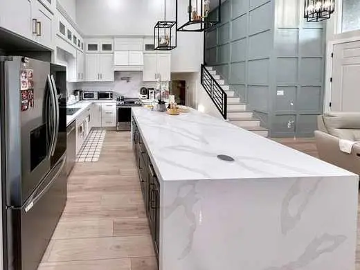 Custom white kitchen with a marble waterfall island and vaulted ceiling, viewed from the dining area