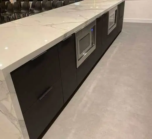 Custom dark charcoal cabinetry kitchen island with a marble waterfall countertop and built-in microwave