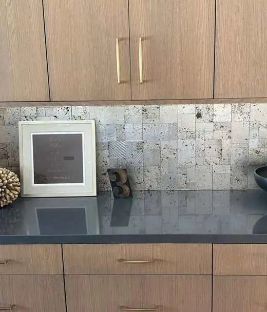 Custom wood-tone slab cabinets with a black quartz countertop, travertine mosaic backsplash, and gold hardware