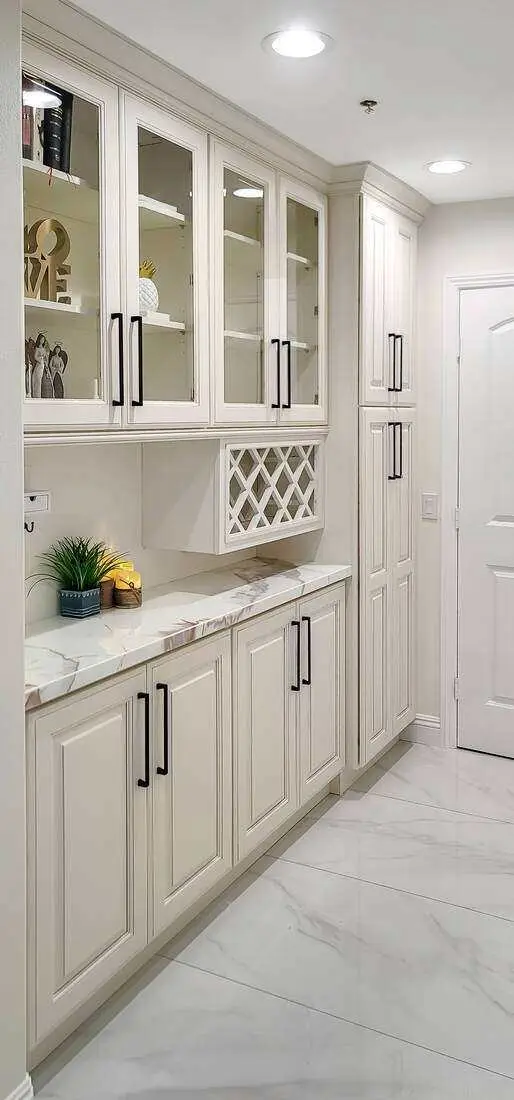 Custom cream built-in hutch with glass-front upper doors, black hardware, and a marble countertop