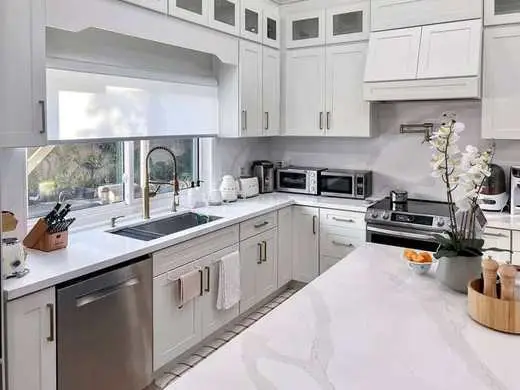 Custom white kitchen with a matte black faucet, marble countertops, and stainless appliances