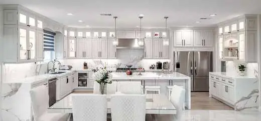 Custom white luxury kitchen with a large marble island, nickel hardware, and pendant lighting