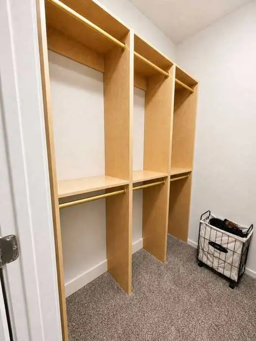 Custom natural oak closet system with brushed gold hanging rods and open shelving