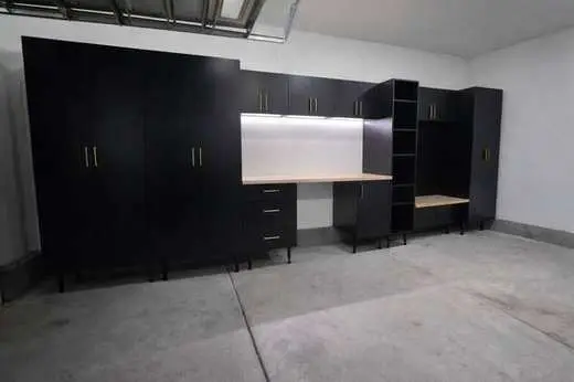 Custom black garage cabinets with gold handles, open shelving, and a built-in workbench