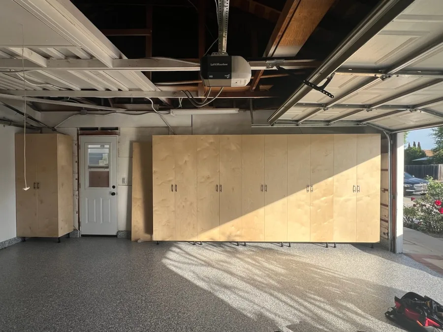 Custom birch plywood garage cabinets on adjustable legs along a full garage wall with an epoxy flake floor