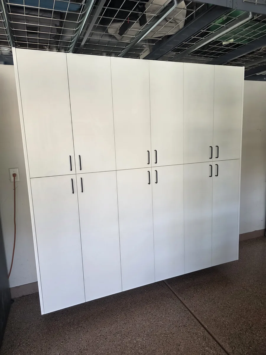Custom white floor-to-ceiling garage cabinets with black pulls above an epoxy flake floor