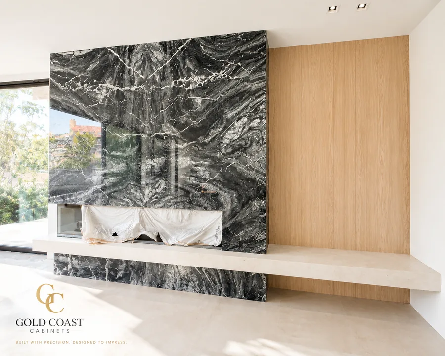 Custom white oak wall paneling with a black marble fireplace surround and floating stone bench in Newport Beach, CA