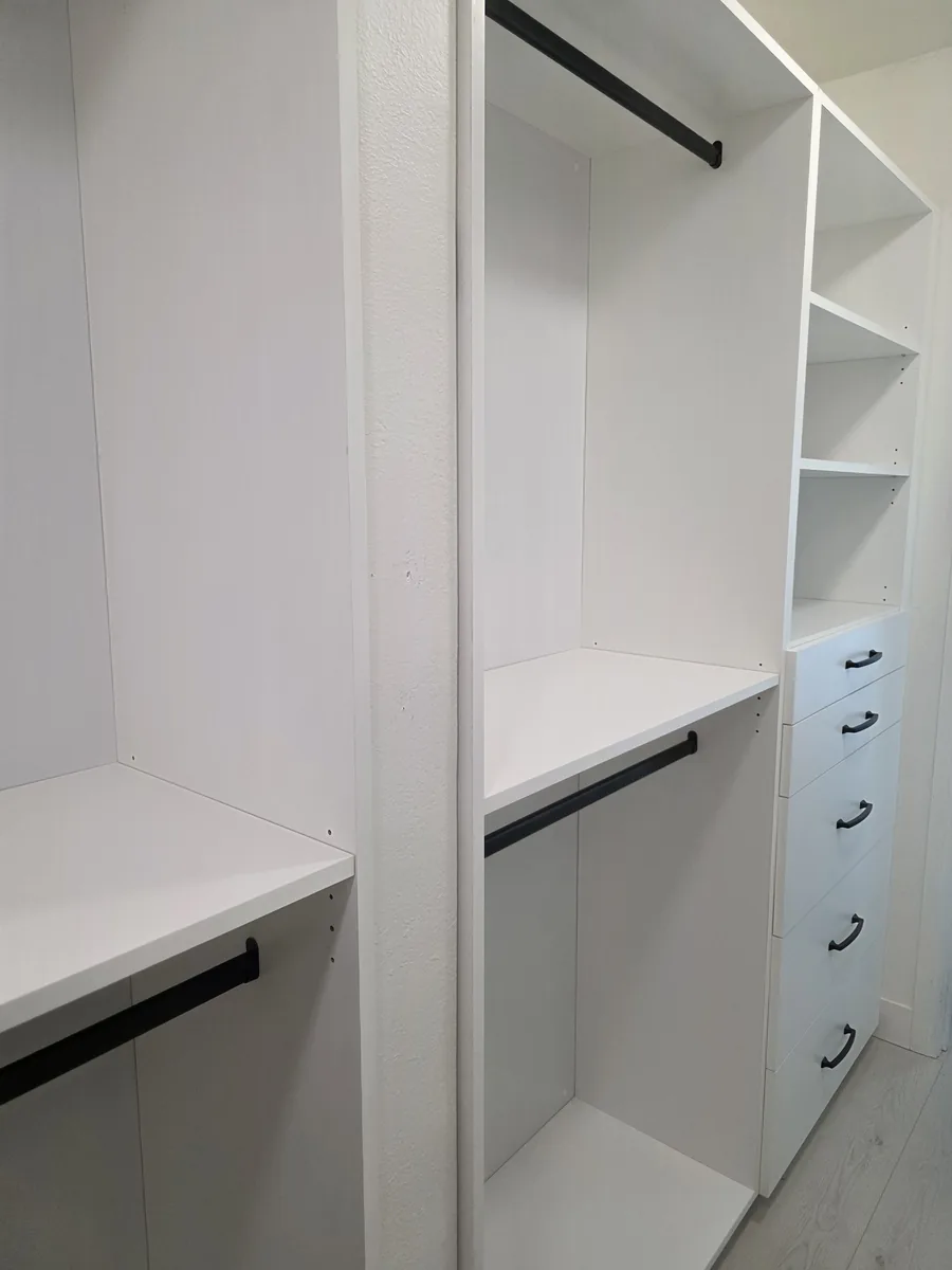 Custom white walk-in closet with double hanging, adjustable shelves, and a drawer stack with black pulls